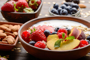 Fruit healthy muesli with peaches strawberry almonds and blackberry in clay dish with yogurt on wooden kitchen table