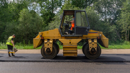 Asphalt roller machine and shovel worker. Road repair works on the suburb highway