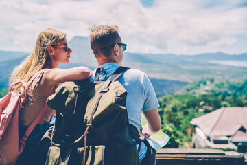 Romantic couple in love spending honeymoon actively hiking with rucksacks exploring nature of island,back view of male and female hipsters looking at beautiful environment resting during hiking tour