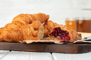 Fresh croissants with berry jam on dark wooden board