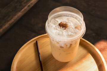 Iced coffee with milk bubble and chocolate powder on top put on wooden tray.