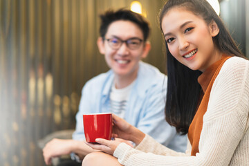 happiness young asian couple marry family enjoy tv show and good conversation embrace together hand hold coffee drink laugh smile together on sofa couch in living room home interior background