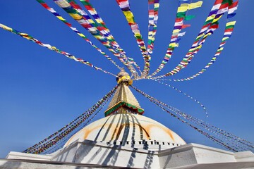 Bodnath Stupa in Kathmandu close up view on bright blue clear sunny sky background. Traditional buddhist architecture. Buddhist symbols. Ancient Buddhist Stupa and prayer flags in Nepal in sunny day.