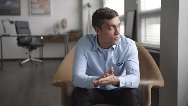 young stressed businessman sits in armchair in office. speaks emotionally, gesticulates actively. looks troubled and indignant, because of problems. has consultation with psychologist. looks in camera