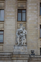Fototapeta na wymiar MOSCOW / RUSSIA - 20/04/2019 soviet communist stone sculpture of a sitting mother holding a baby child (sculptors Baburin, Nikogosyan, Anikushin) Kudrinskaya Square Building (Aviators' House) facade