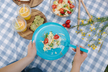 Woman take salad from blue plate on vegan picnic outdoors. Fresh and healthy food. First person view