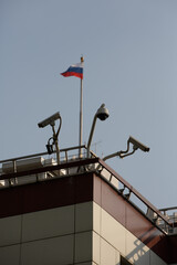 vertical day shot of three cctv surveillance cameras on the walls of the Parlament and a flag of Russia on a blue sky background