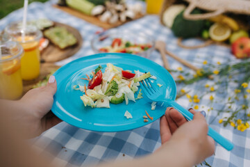 Woman take salad from blue plate on vegan picnic outdoors. Fresh and healthy food