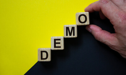 Wood cubes with word 'demo' stacking as step stair on paper black and yellow background, copy...