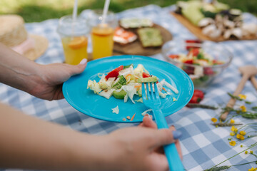 Woman take salad from blue plate on vegan picnic outdoors. Fresh and healthy food