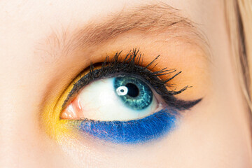 Obraz premium Woman eye looking up. Blue and yellow eyeshadow and black eyeliner arrow make up close up