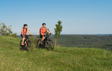 Grandmother with electric mountain bike and granddaughhter without electric help on a smooth meadow trail in the Franconian Switzerland area of Bavaria, Gemany