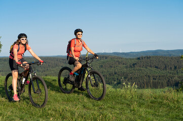Fototapeta na wymiar Grandmother with electric mountain bike and granddaughhter without electric help on a smooth meadow trail in the Franconian Switzerland area of Bavaria, Gemany