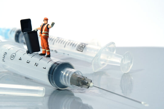 Cleaning workers carry trash bin, standing above syringe that has been used. Medical waste conceptual photo. Miniature people photography.
