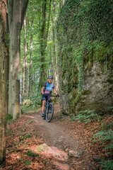 Fototapeta na wymiar pretty senior woman underway on her electric mountain bike on a rocky forest trail in Franconian Switzerland, Bavaria, Germany