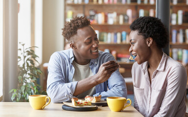 African American guy feeding piece of pie to his girlfriend at cafe
