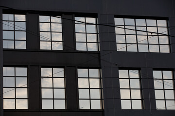 Contrasty abstract filled frame shot of a wall with nine large rectangular windows on a blue sky and white clouds background, forming beautiful geometrical patterns, textures and shapes