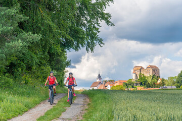 Fototapeta premium grandmother and granddaughter riding their mountain bikes in front of the awesome skyline of Hiltpoltstein in Frankonian Switzerland, Bavaria, Germany