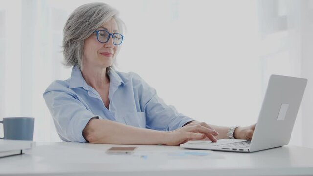 Relaxed senior woman spending time home scrolling web-pages on laptop, success