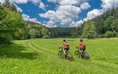 Grandmother with electric mountain bike and granddaughhter without electric help on a smooth meadow...