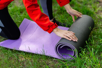 young girl in a red jacket unwinds a yoga mat closeup on summer in nature 