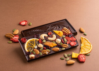 Chocolate dark Belgian bar with the addition of fruit nuts on brown background. Dessert food concept.