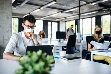 Young people with face masks back at work or school in office after lockdown.