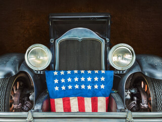 Classic early twentieth century limousine car with the American flag in front of the grille