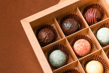 Obraz premium Chocolate candies truffle from various chocolate toppings in a box with a satin ribbon against a dark brown background.