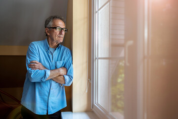 Senior man looking out of window at home
