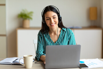 Woman In Headset Making Video Call Sitting At Laptop Indoor - obrazy, fototapety, plakaty