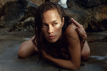 Beautiful suntanned woman posing on a beach. Wet hair, sand on the skin