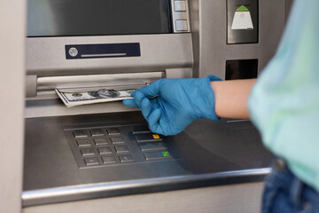 Female hand in protective medical glove taking money from ATM machine