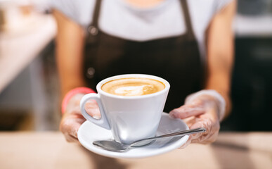 Unrecognizable woman with gloves working in cafe, holding cup of coffee.