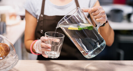 Unrecognizable woman with gloves working in cafe, pouring water.