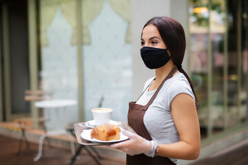 Young woman with face mask working in cafe, serving customers.