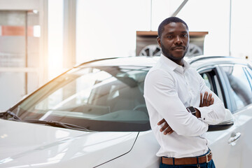 portrait of happy handsome african man in car dealership, afro man came to buy beautiful luxurious...