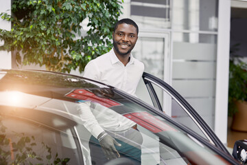 portrait of happy handsome african man in car dealership, afro man came to buy beautiful luxurious...