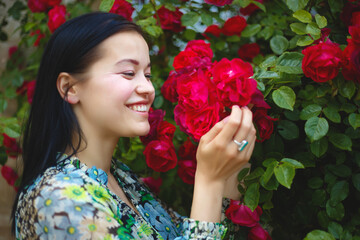 Obraz na płótnie Canvas brunette woman smiling in a flowering bush of red roses