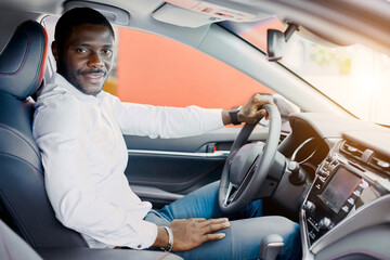 handsome rich african man try himself behind the wheel of new automobile, man likes it, gong to buy