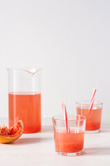 Summer refreshing grapefruit drink, jug and glasses with grapefruit pulp and juice and straws
