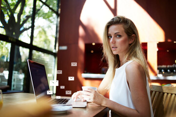 Portrait of a young attractive female creative designer sitting with laptop computer in modern cafe interior, beautiful woman freelancer using net-book. Infographics elements of email envelope sings