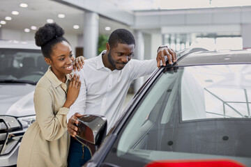 black african couple liked a car in dealership, they want to buy it, discuss together - obrazy, fototapety, plakaty