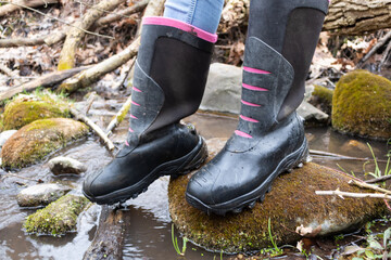 Hiker standing on a rock in a stream wearing tall boots.
