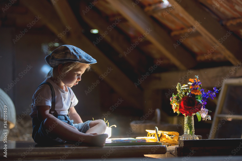 Poster Cute beautiful child, blond kid, reading book and playing with construction blocks in a cozy attic room