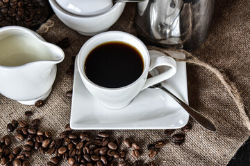cup of coffee in a white coffe Cup with milk jug  and Sugar pot and roasted coffee Beans