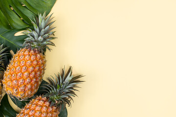 Fototapeta premium Beautiful pineapple on tropical palm monstera leaves isolated on bright pastel yellow background, top view, flat lay, overhead above summer fruit.