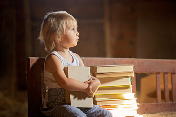 Fototapeta na wymiar Little toddler boy, sitting on old vintage bench, holding books in attic