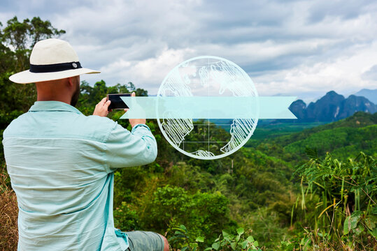 Back view of man wanderlust photographing subtropical jungle forest on smartphone camera. Young hipster guy is taking photo on cell telephone. Discovering world in travel. Infographics earth symbol
