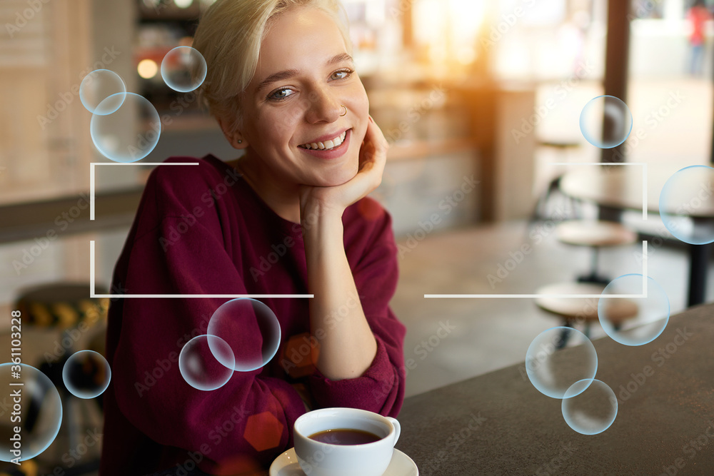 Wall mural portrait of caucasian smiling female sitting in coffee shop interior with cup of tasty cappuccino. b